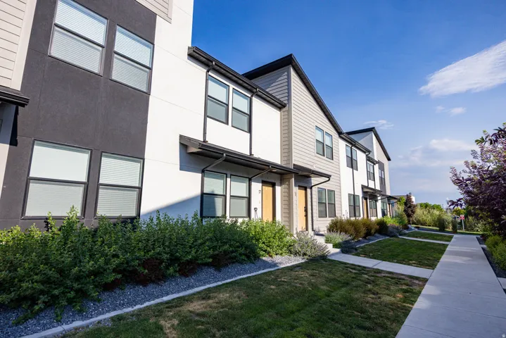 Modern multi-story facade featuring mixed siding, prominent window placement, mature landscaping, concrete walkways, and awnings