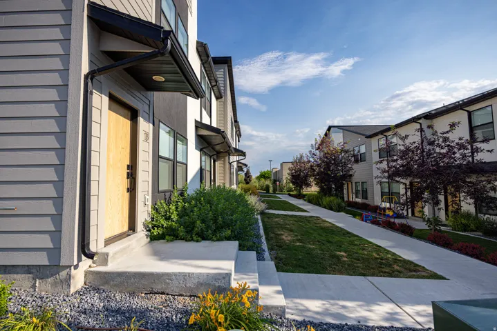 Contemporary townhome exterior featuring light gray siding and a natural wood-finish entry door