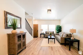 Bright living area featuring wood-finish flooring, recessed lighting, a staircase with black metal balusters, and a solid wood entry door