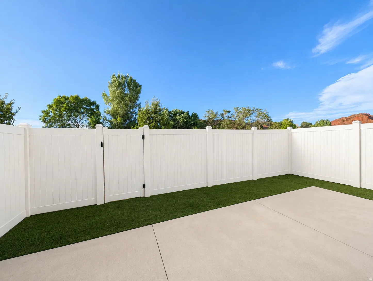 Private fenced yard featuring a concrete patio, artificial turf, and white panel fencing with a gate