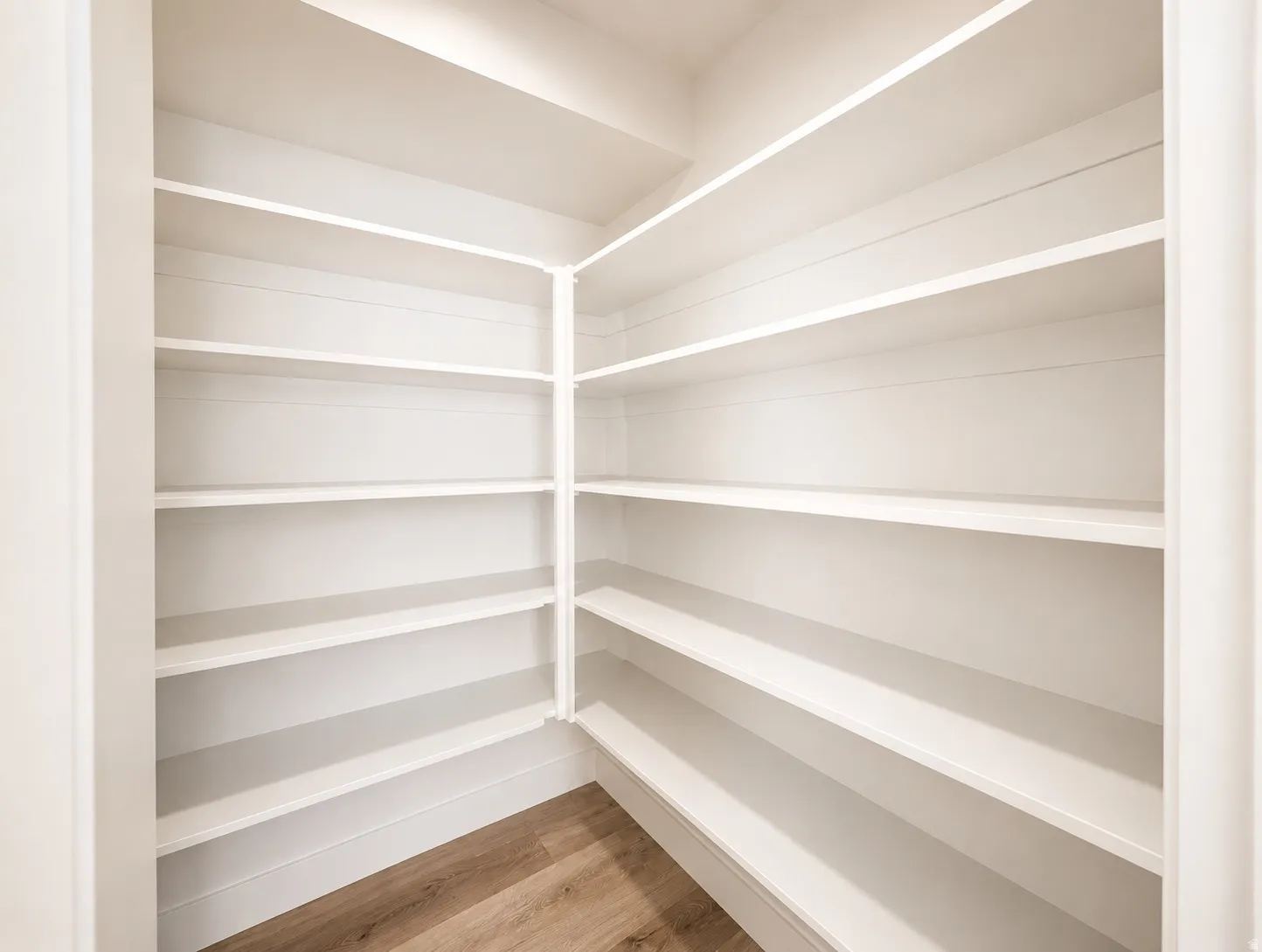 Walk-in pantry featuring extensive white shelving and wood-finish flooring