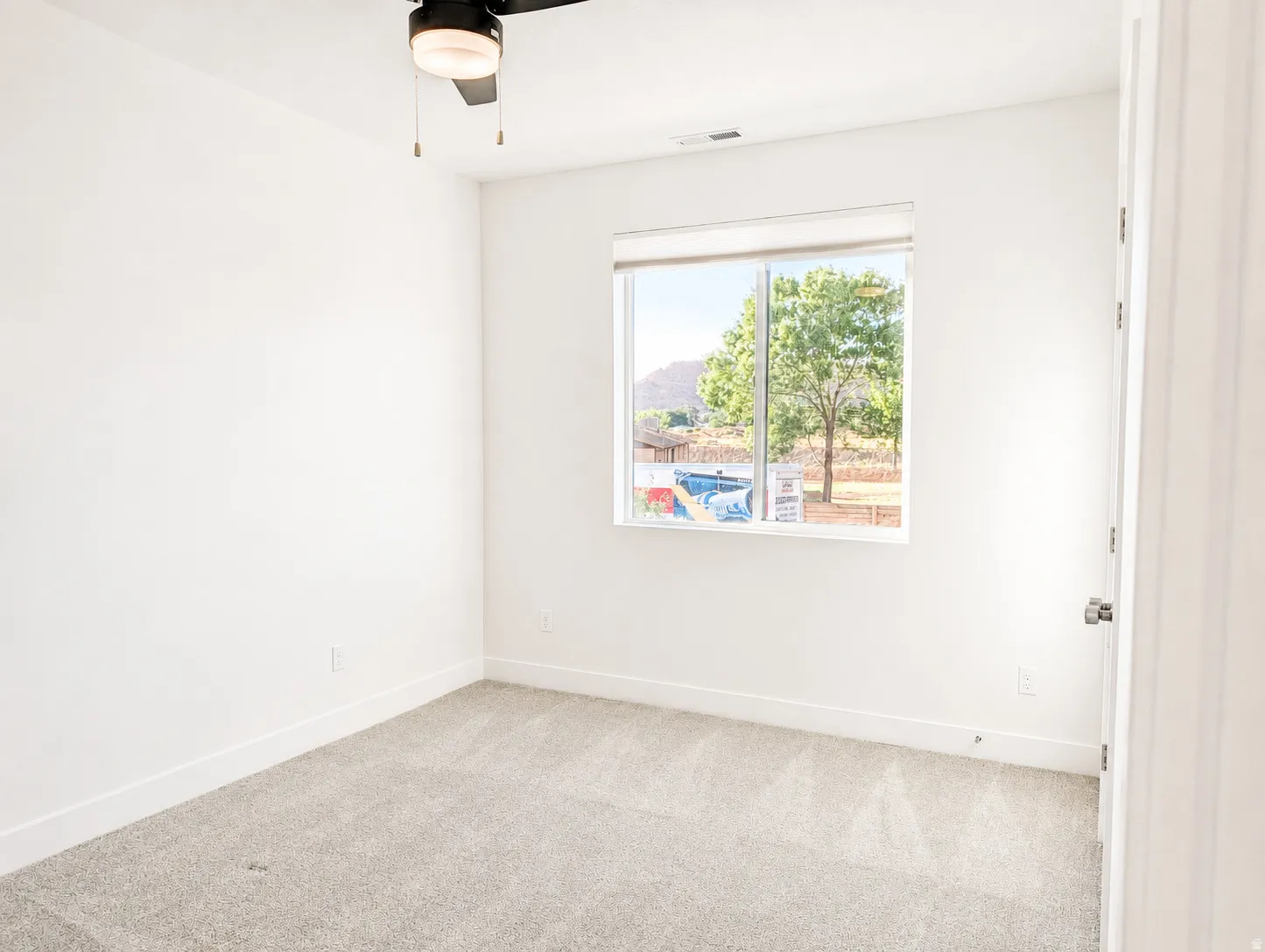 Light-filled room featuring a broad window, neutral-toned carpet, white walls, and a contemporary ceiling fan with integrated lighting
