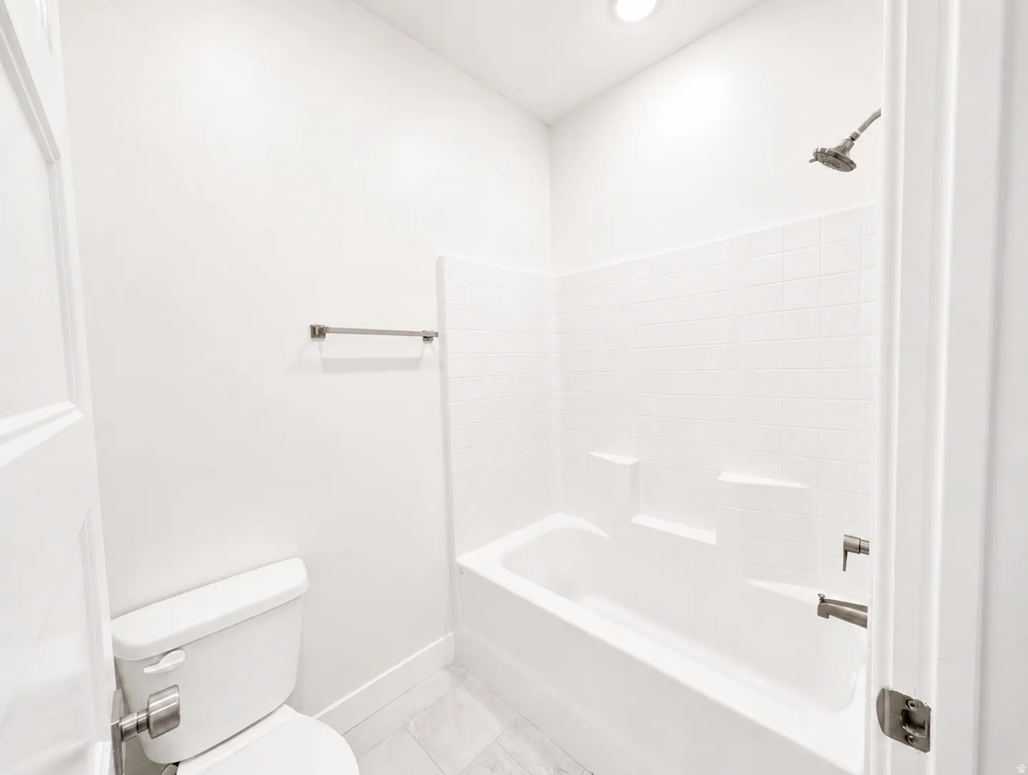 Bathroom featuring a white bathtub, shower with brushed nickel fixtures, white subway tile surround, white toilet, and light gray tile flooring
