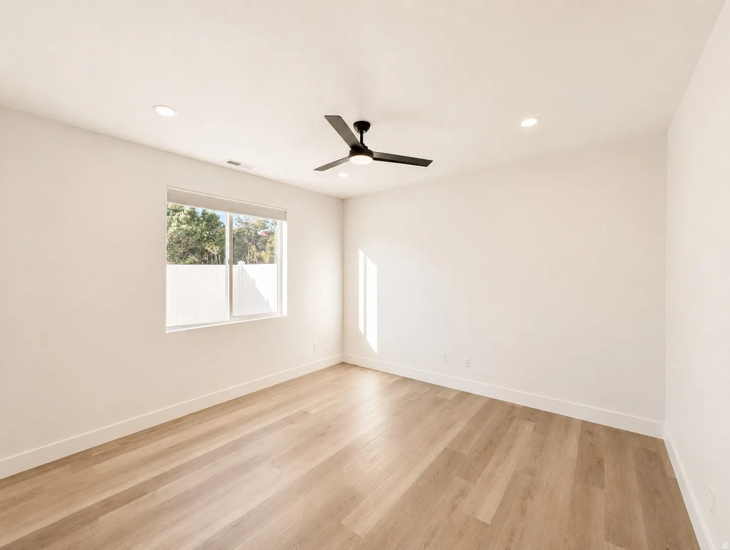 Spacious room with light wood-finish flooring, recessed lighting, and a modern ceiling fan