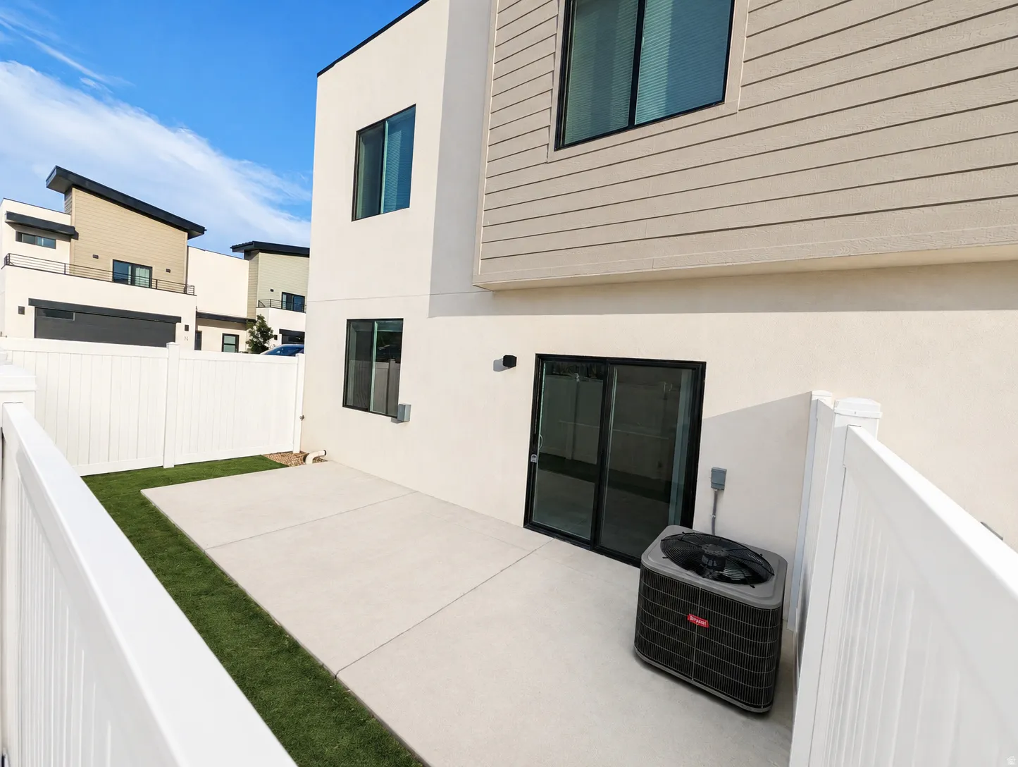 Private outdoor space featuring a concrete patio and artificial turf area, enclosed by white vinyl fencing