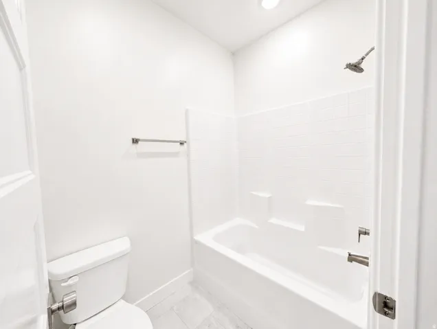 Bathroom featuring a white bathtub, shower with brushed nickel fixtures, white subway tile surround, white toilet, and light gray tile flooring