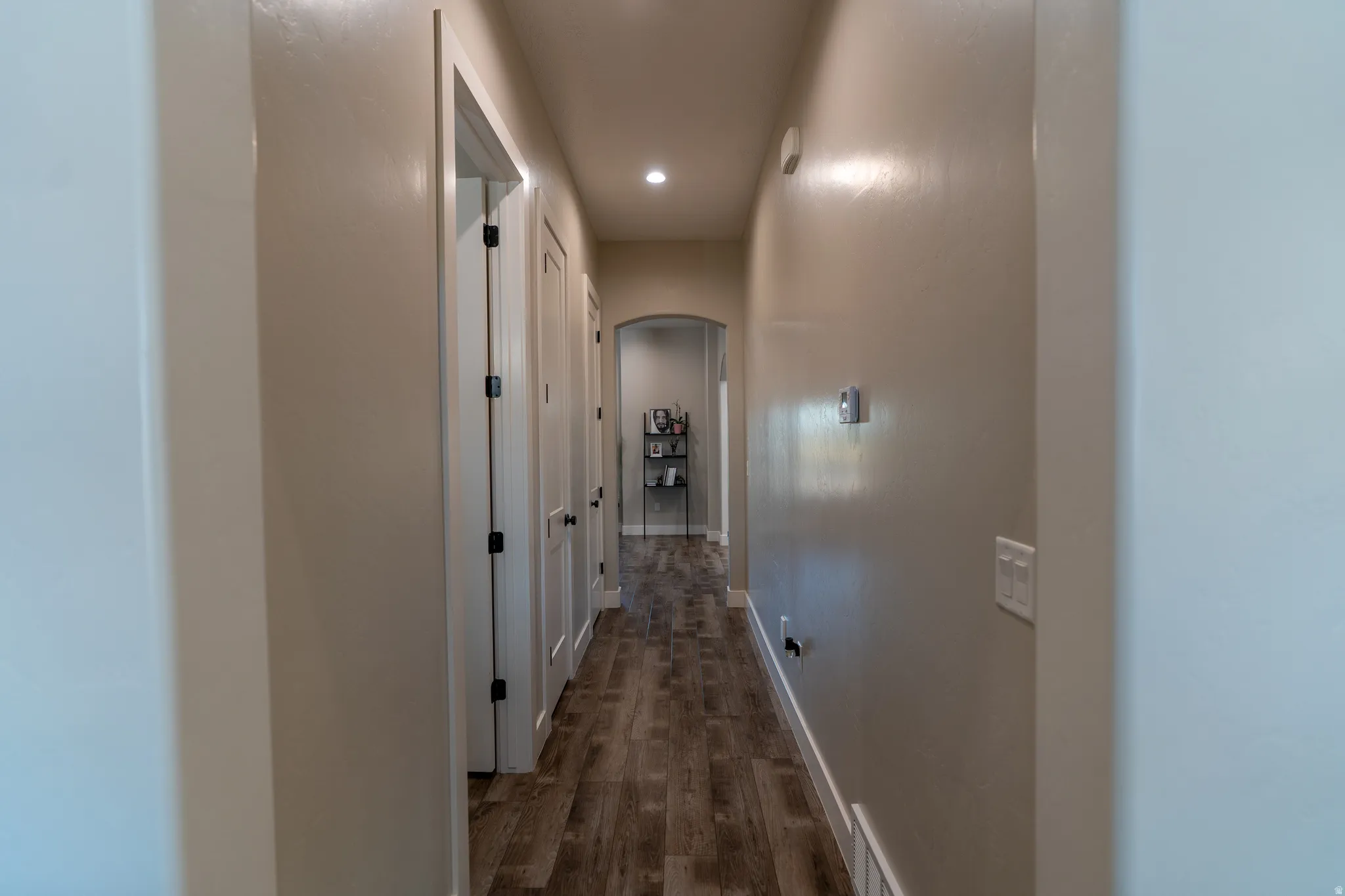 Hallway featuring wood-finish flooring, recessed lighting, and an arched doorway