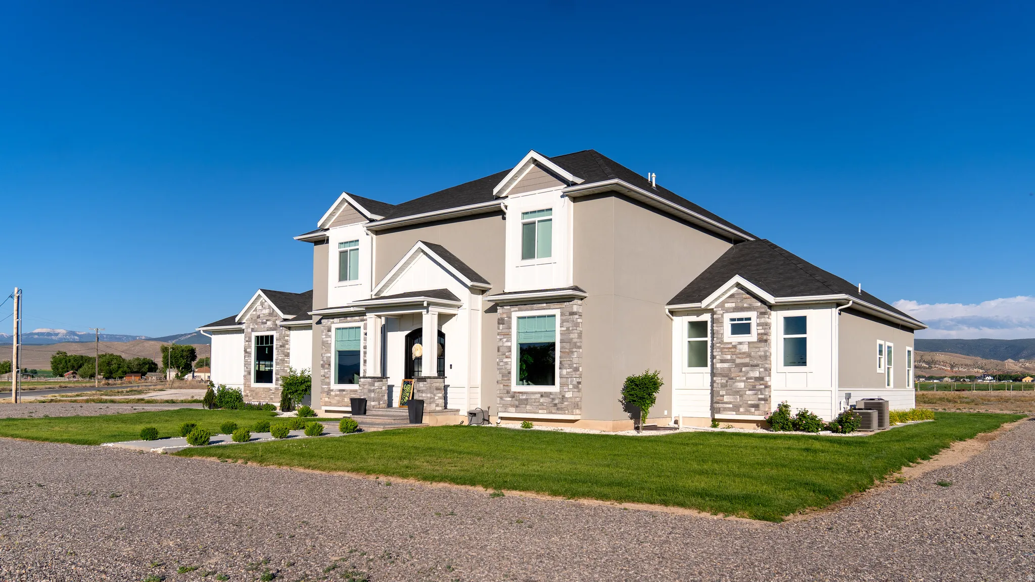 Two-story residence featuring light gray stucco siding and stone veneer accents