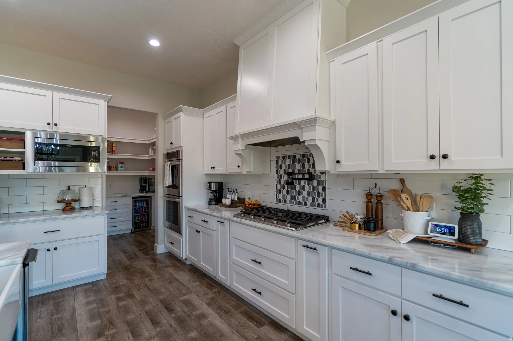Kitchen featuring white shaker cabinetry, stainless steel appliances, wood-finish flooring, white subway tile backsplash, and light-toned countertops