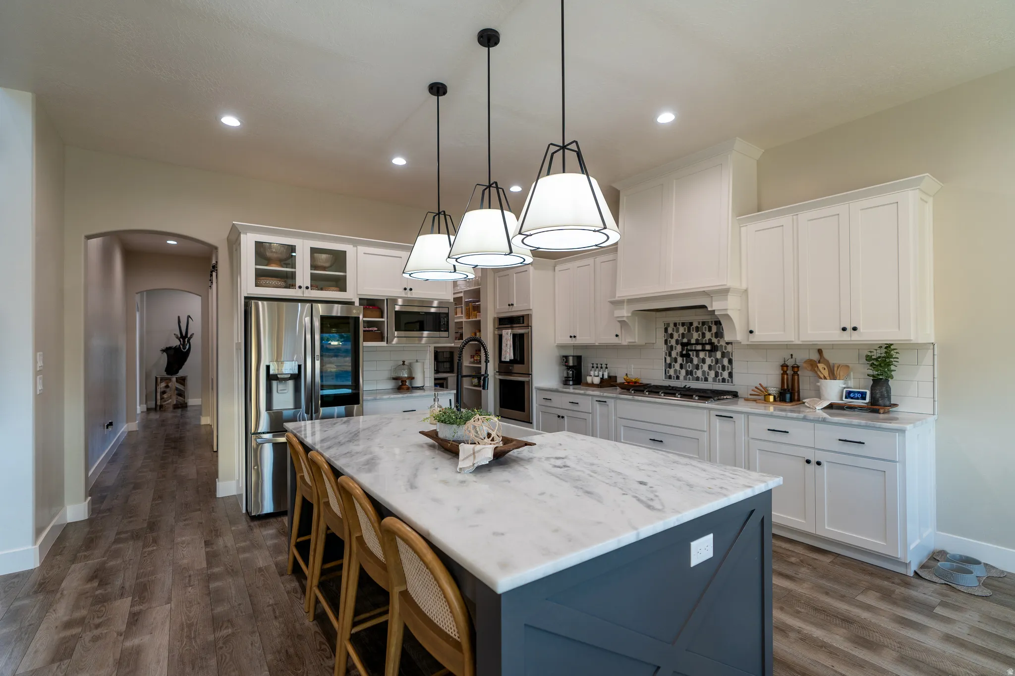 Spacious kitchen featuring an oversized island with countertop seating, white shaker-style cabinetry, stainless steel appliances, and wood-finish flooring