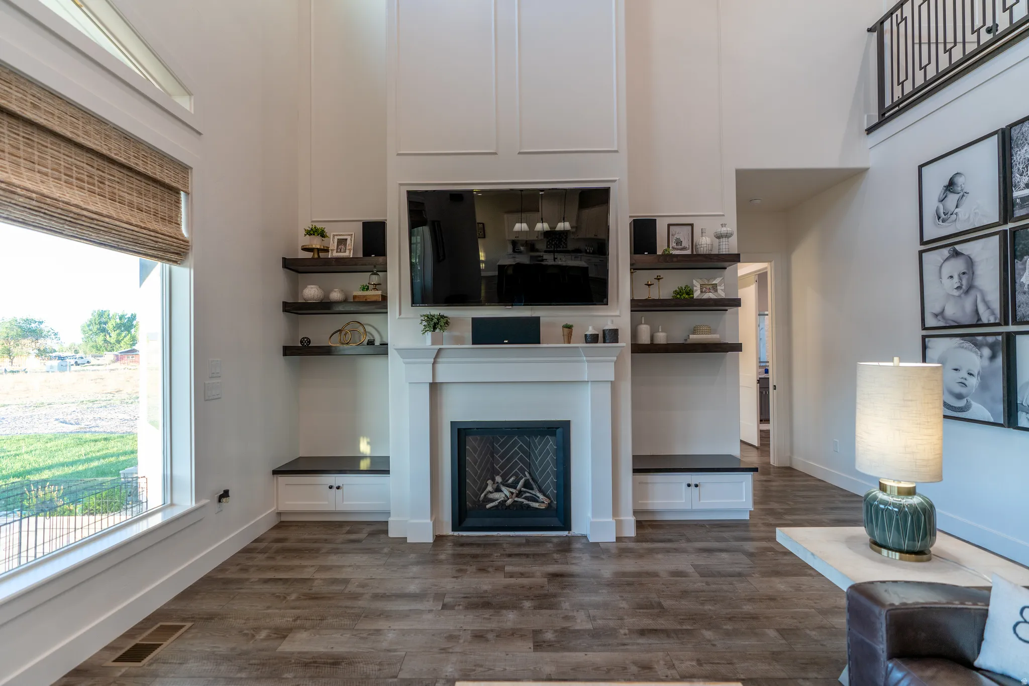 Living area featuring a floor-to-ceiling fireplace with an integrated media center, soaring ceilings with architectural detailing, wood-finish flooring, and a large picture window