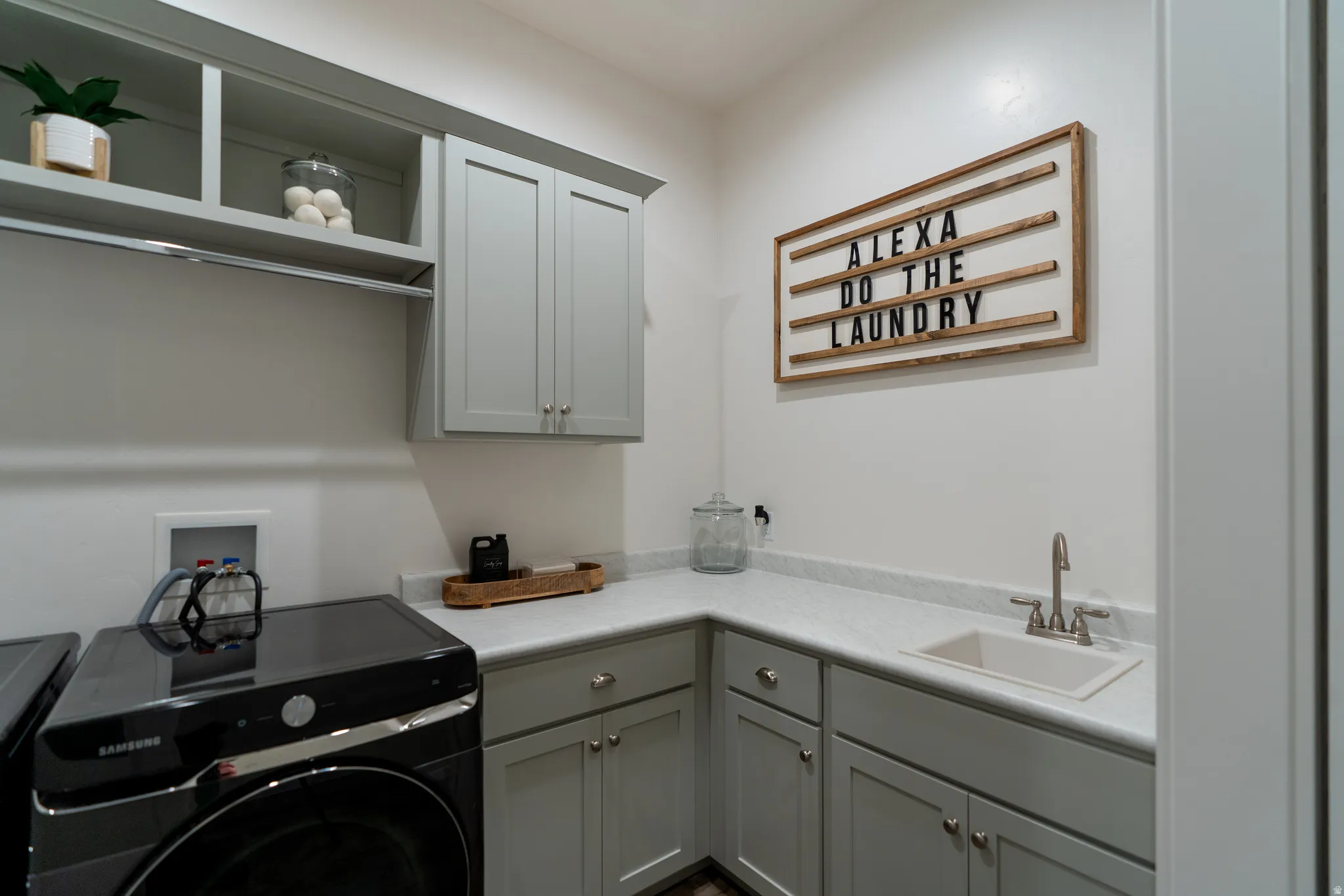 Laundry room featuring light gray cabinetry, white countertops, built-in sink, and integrated clothes hanging rod