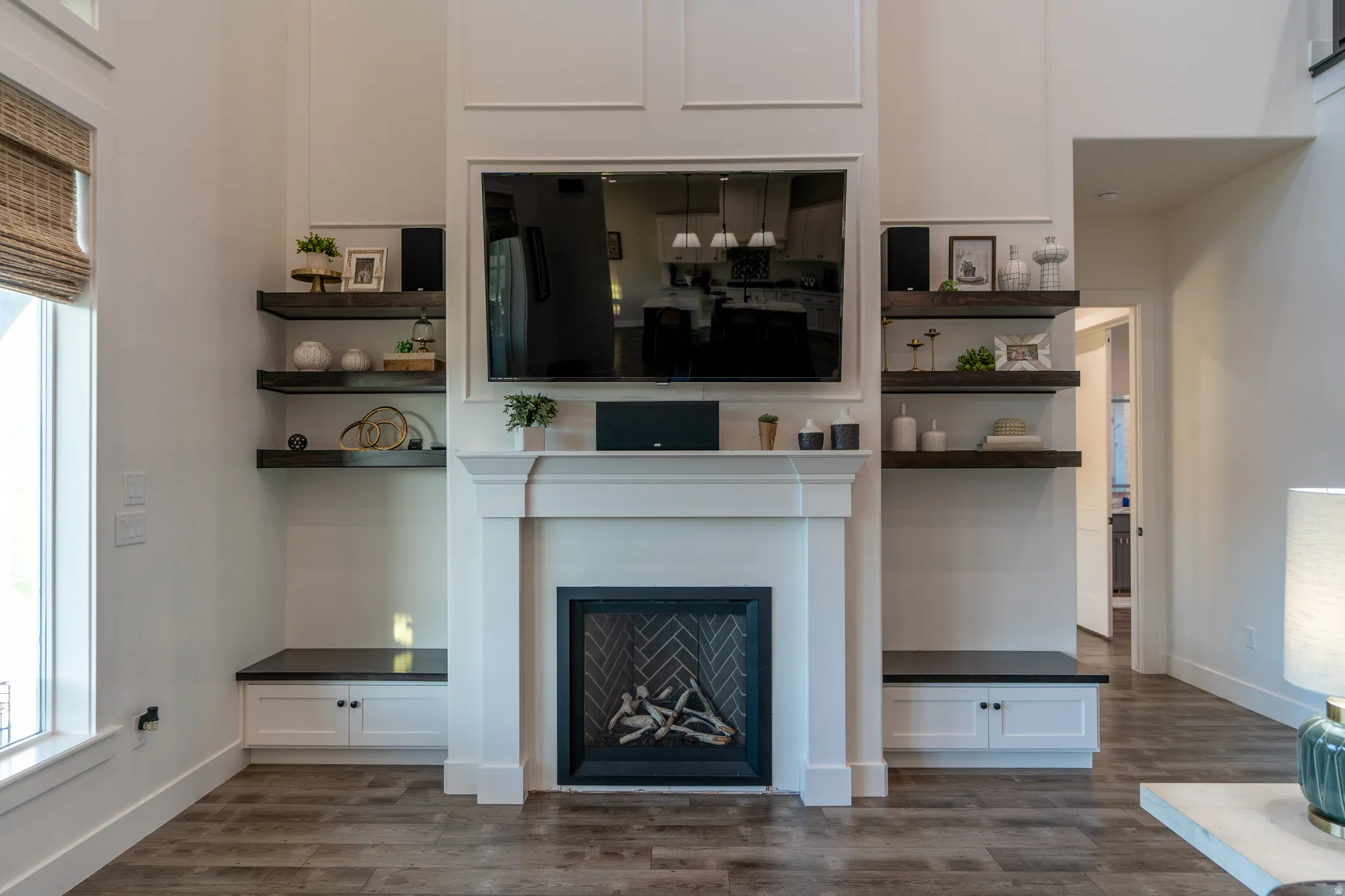 Modern living room featuring a tall white fireplace surround, built-in shelving, integrated lower cabinetry, and wood-finish flooring