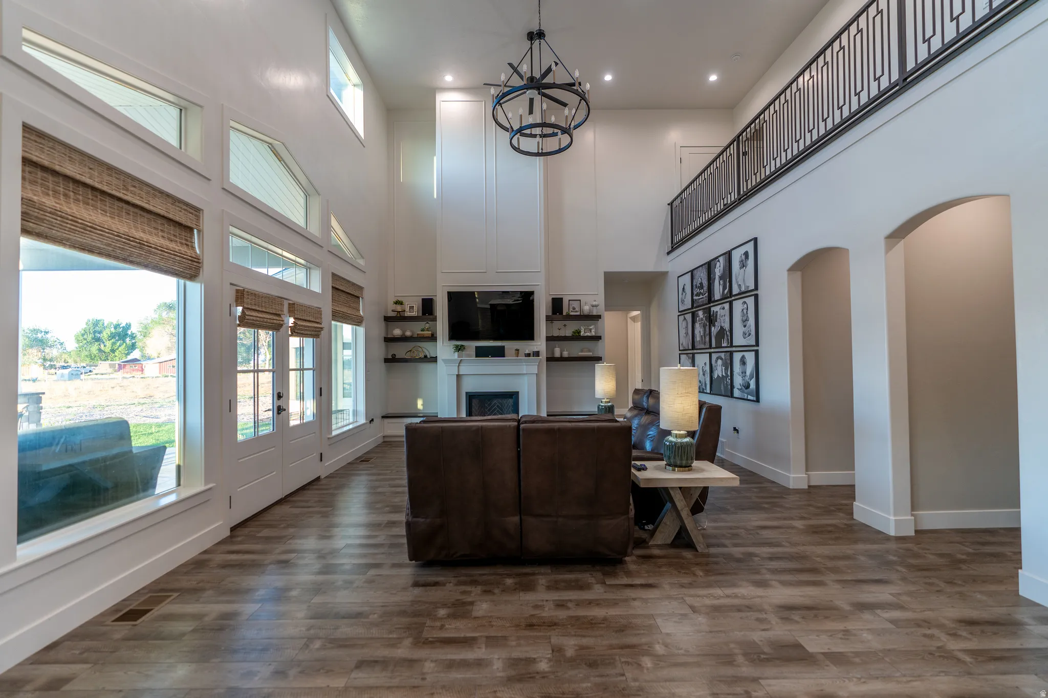 Spacious living area featuring high ceilings with a tiered chandelier, wood-finish flooring, and a fireplace with a mantelpiece