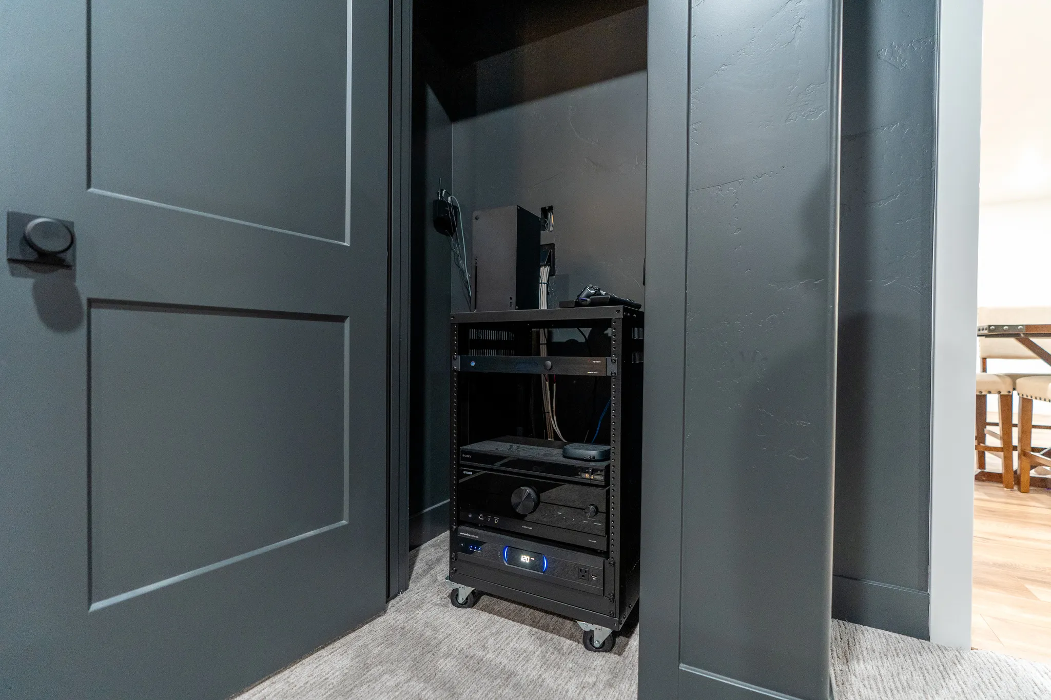 Media closet featuring a black AV rack on casters, dark paneled walls, and a recessed ceiling
