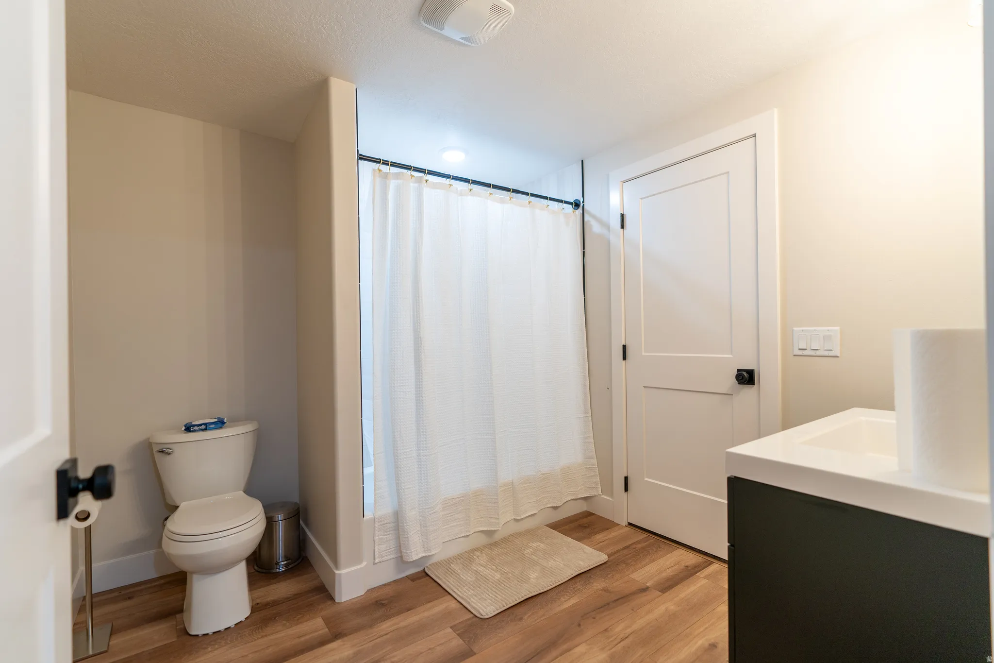 Full bathroom featuring wood-finish flooring, a white toilet, a shower with a white curtain, a flat-panel door with matte black hardware, and a vanity with a white countertop
