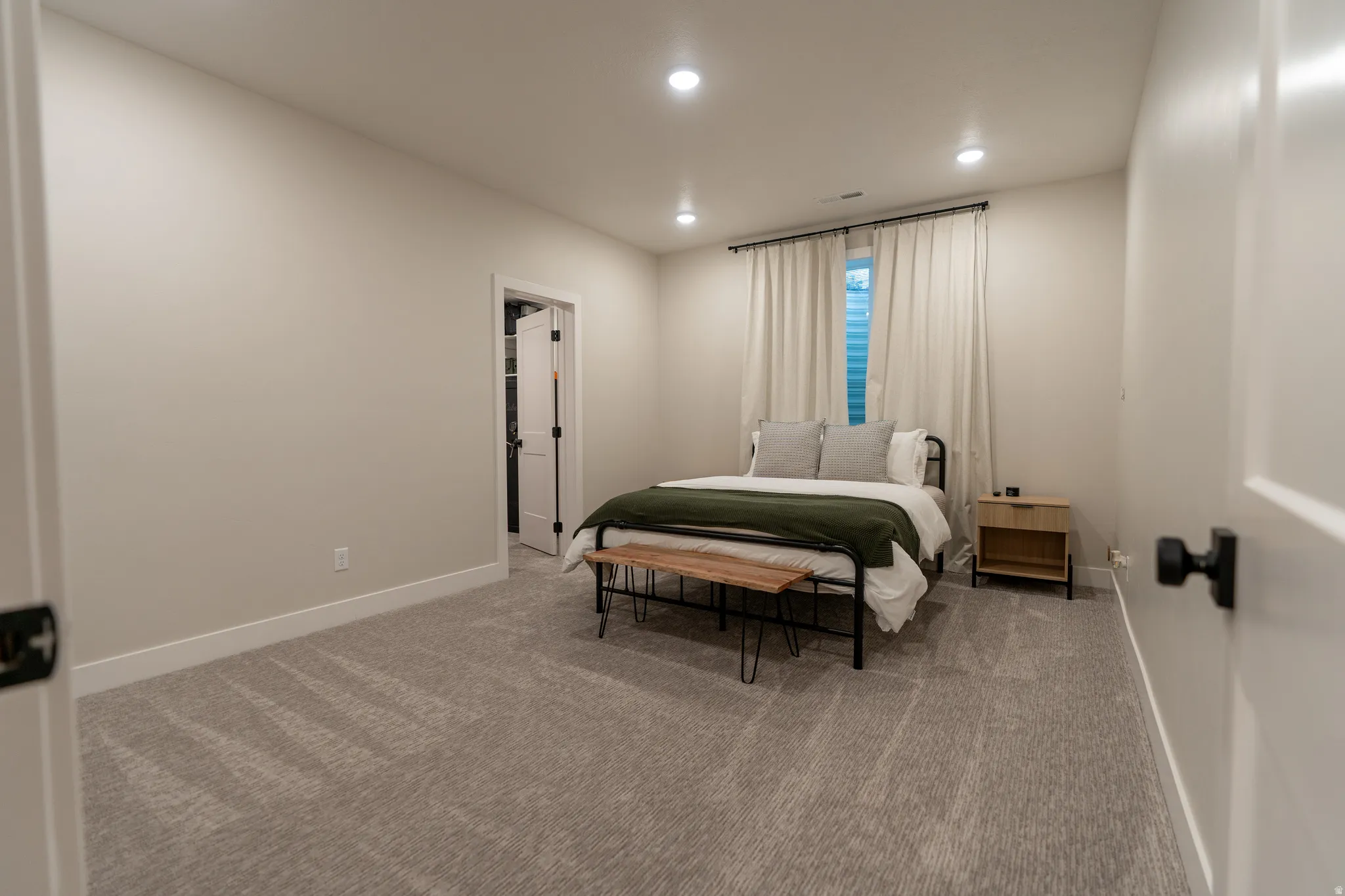 Carpeted room featuring recessed lighting, a window with curtains, and a doorway leading to a walk-in closet