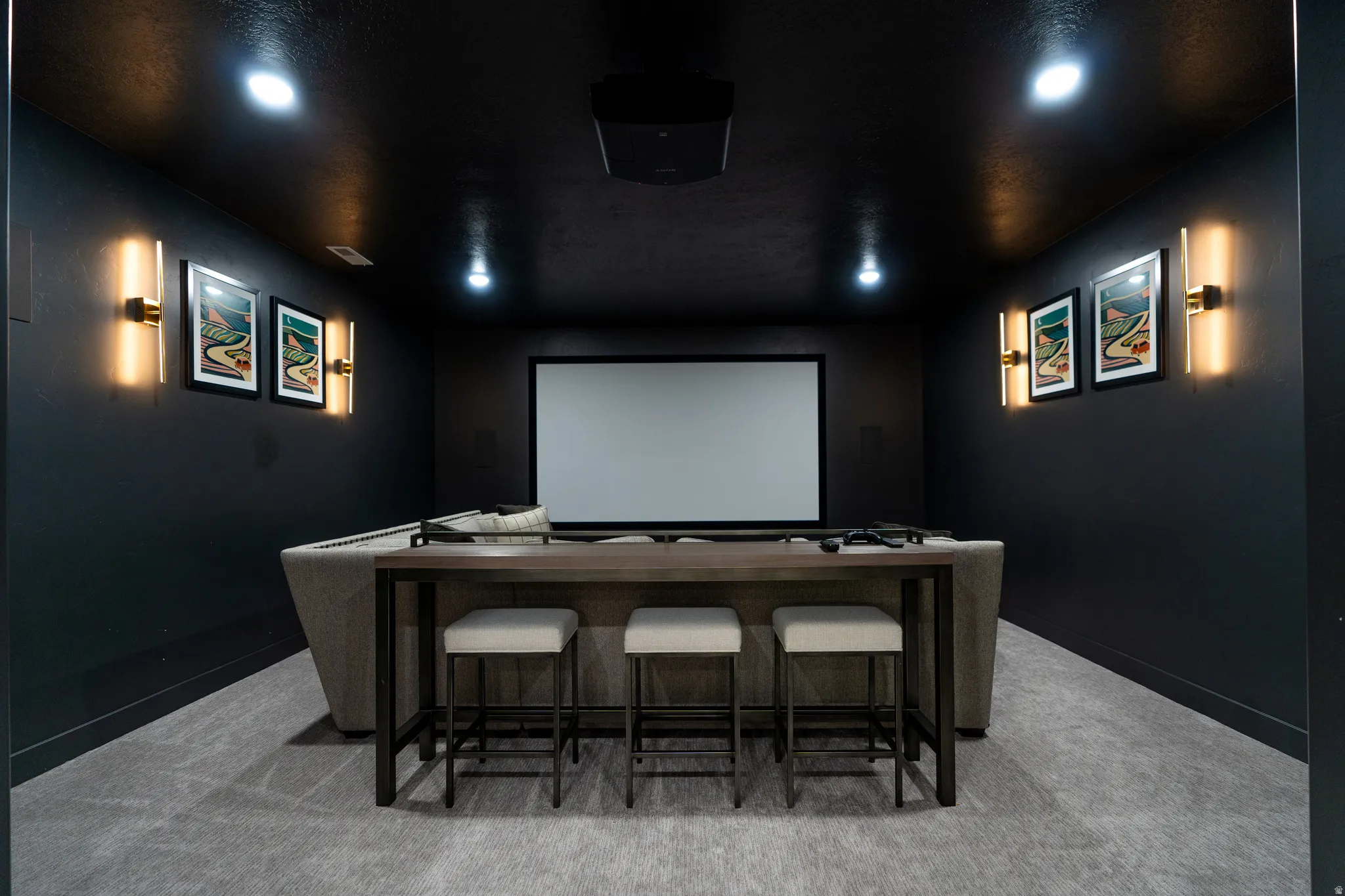 Dedicated media room featuring a large projection screen, dark-toned walls, recessed ceiling lighting, and wall-mounted sconces