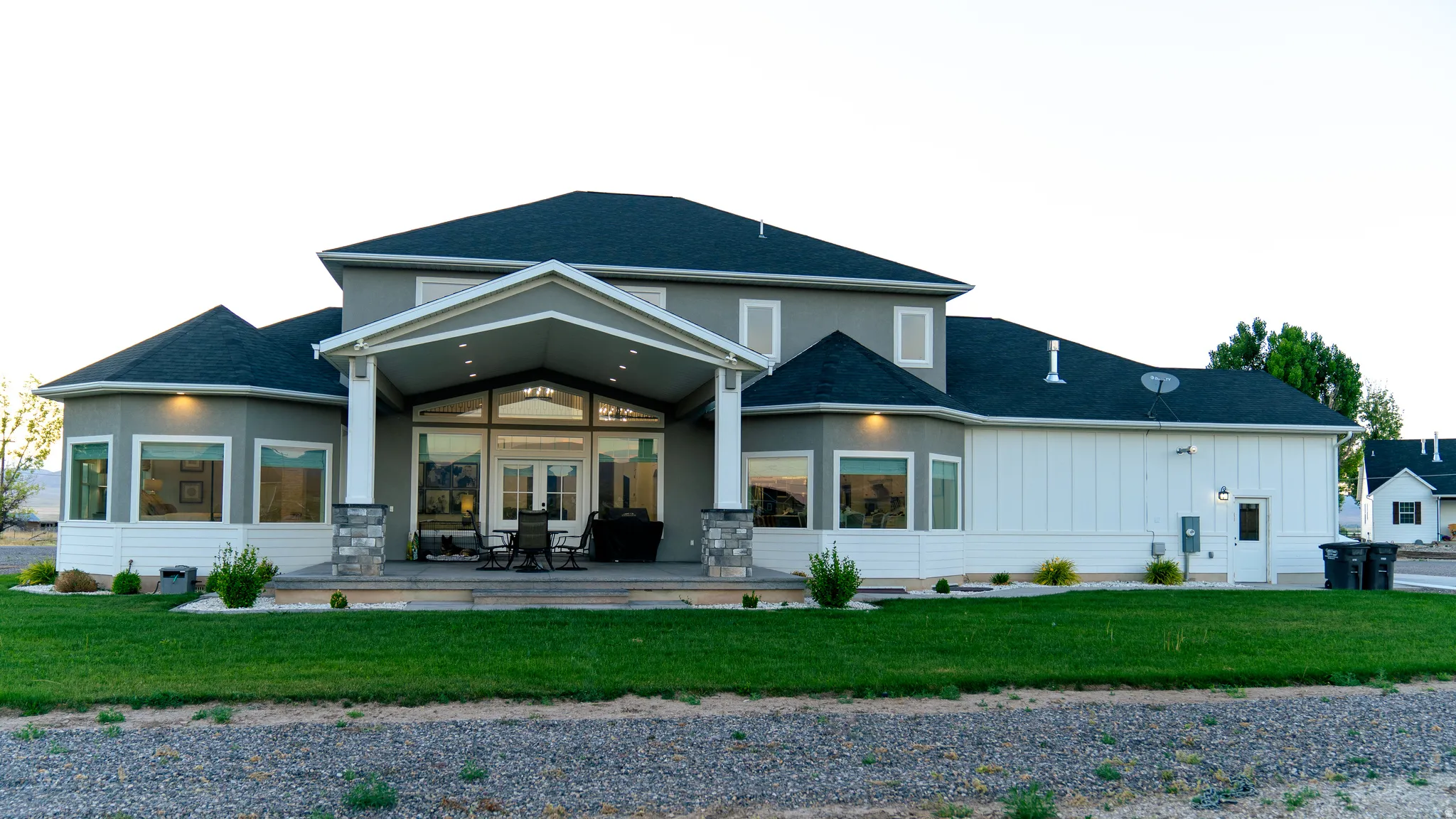Rear exterior featuring a covered patio, multiple large windows, a bay window section, and a manicured lawn