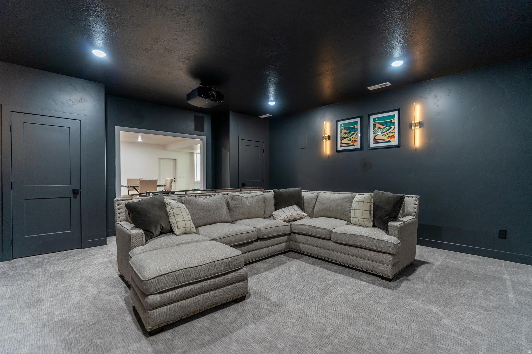 Dedicated media room featuring recessed lighting, a ceiling-mounted projector, wall sconces, and neutral-toned carpeting