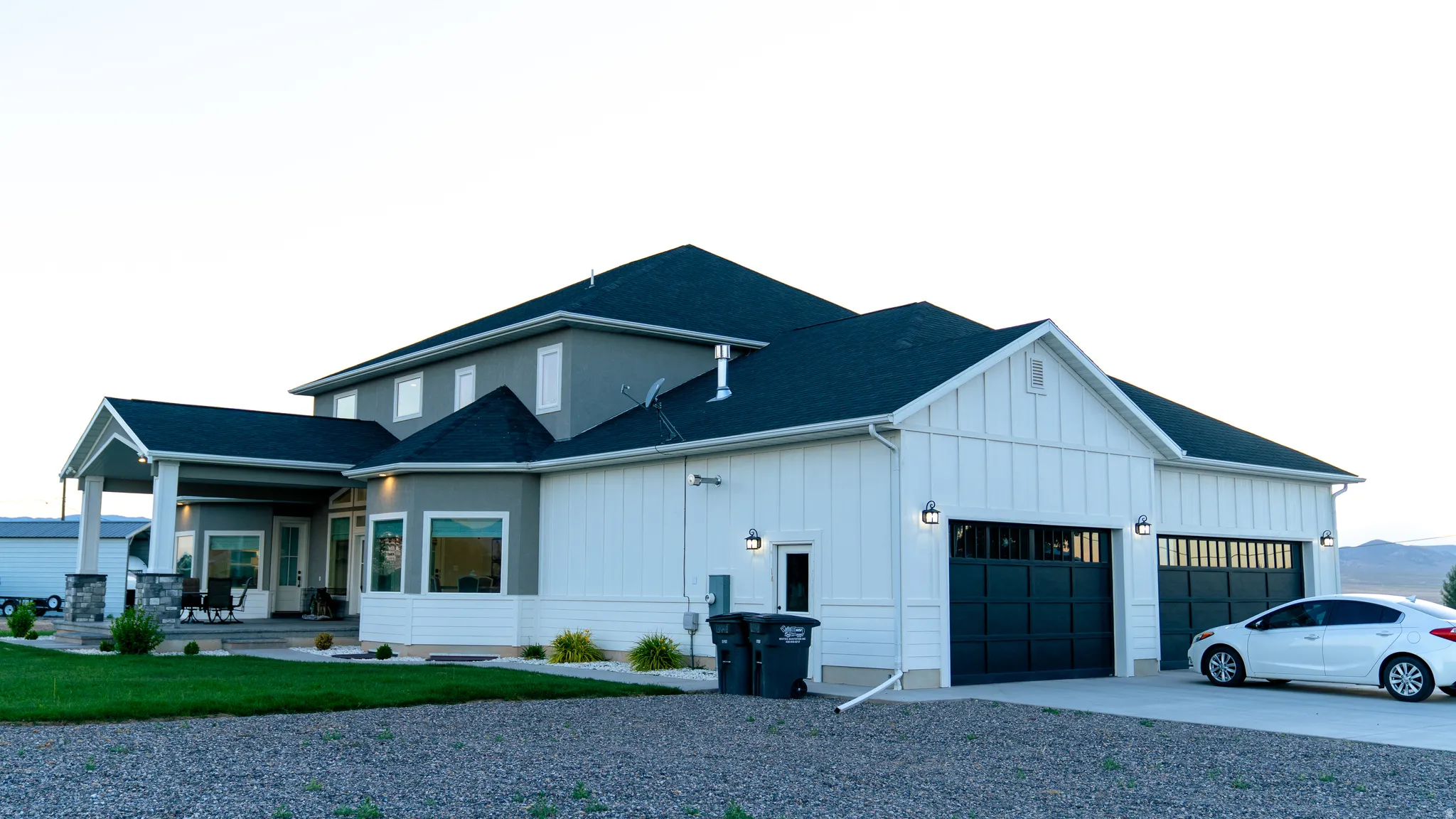Contemporary two-story residence featuring a dark shingle roof, gray stucco siding, and white vertical paneling