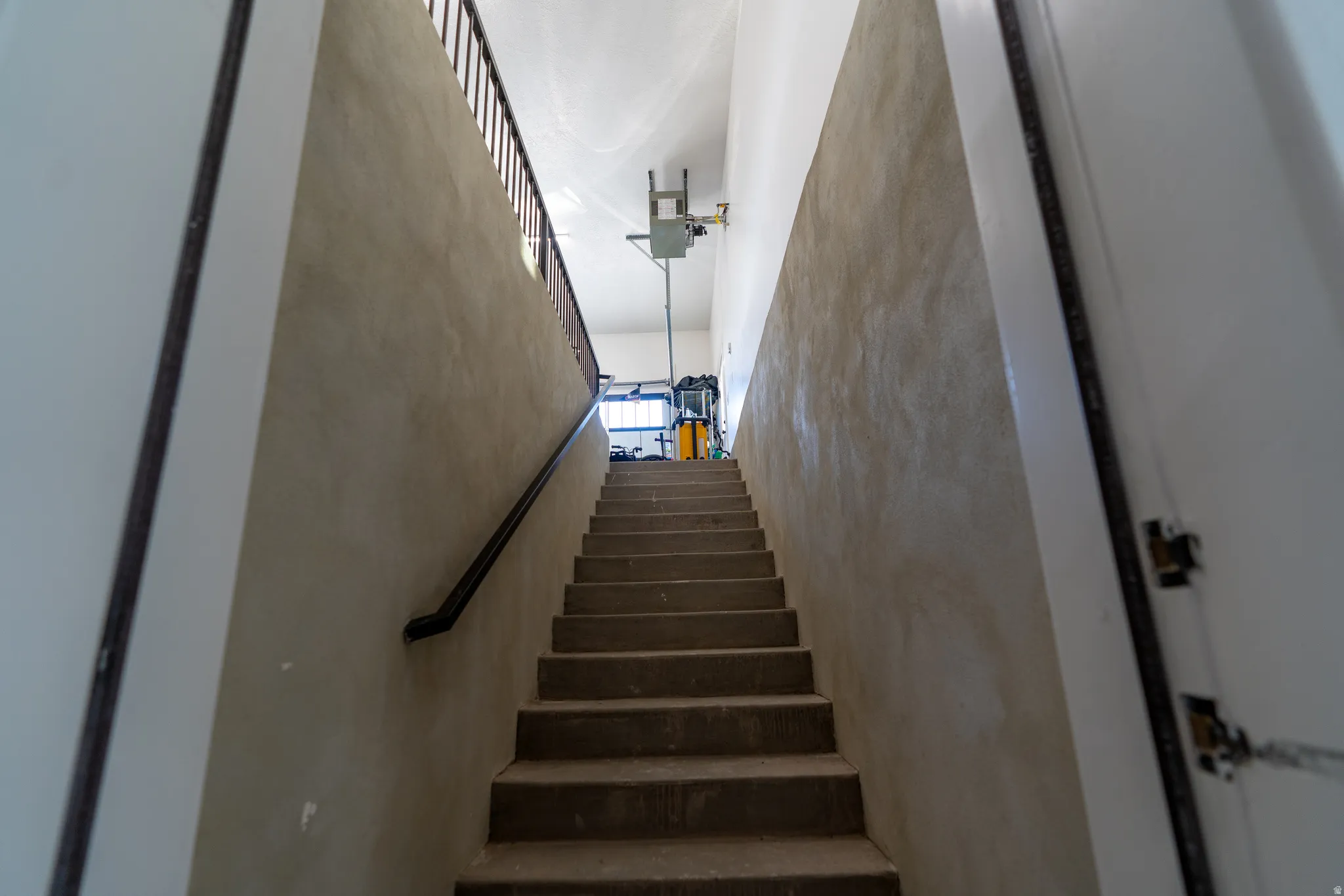 Stairwell featuring concrete steps, a black handrail, and a textured wall finish