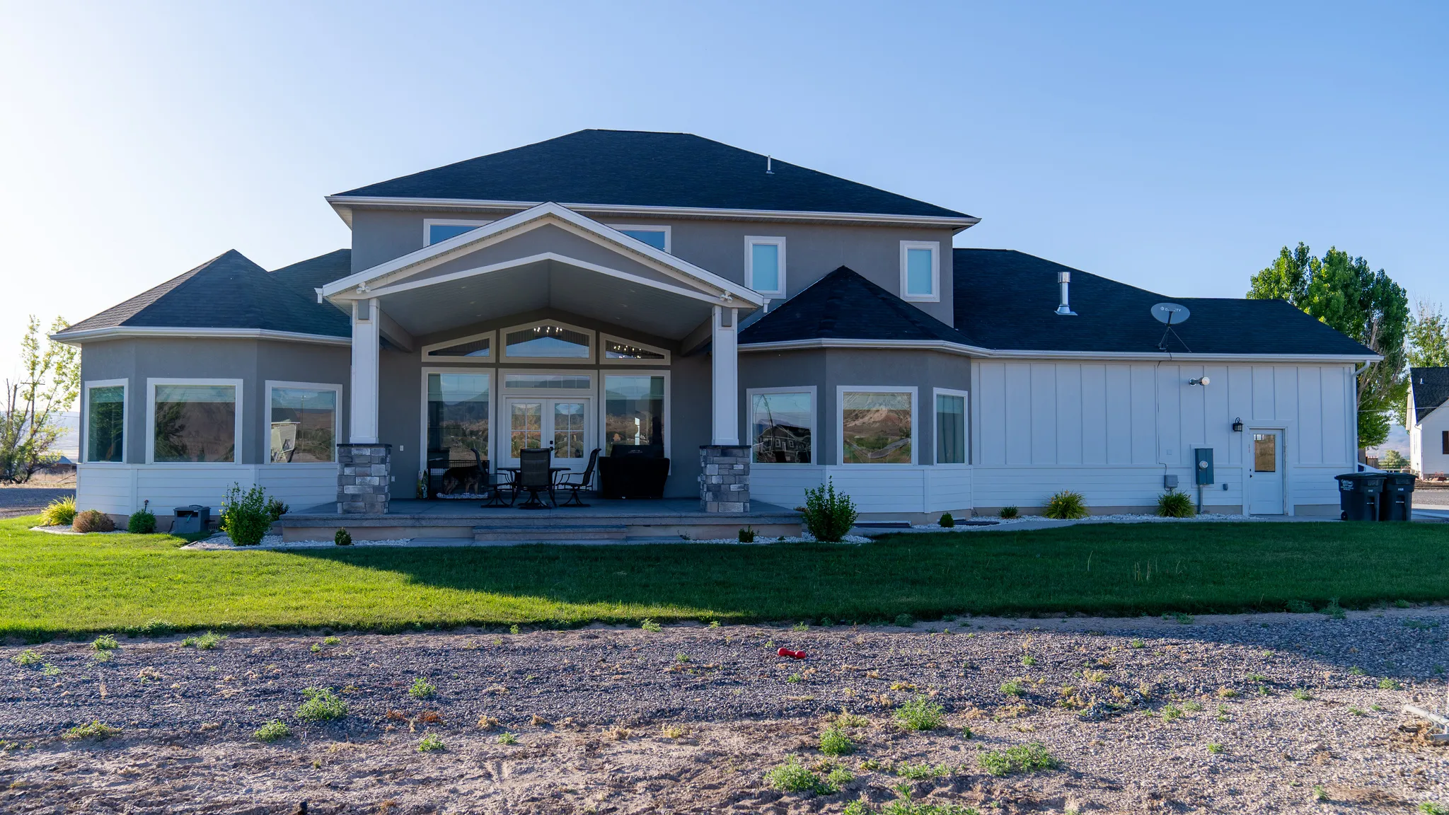 Rear elevation featuring a covered patio with stone-accented columns, extensive glass doors, and a manicured lawn