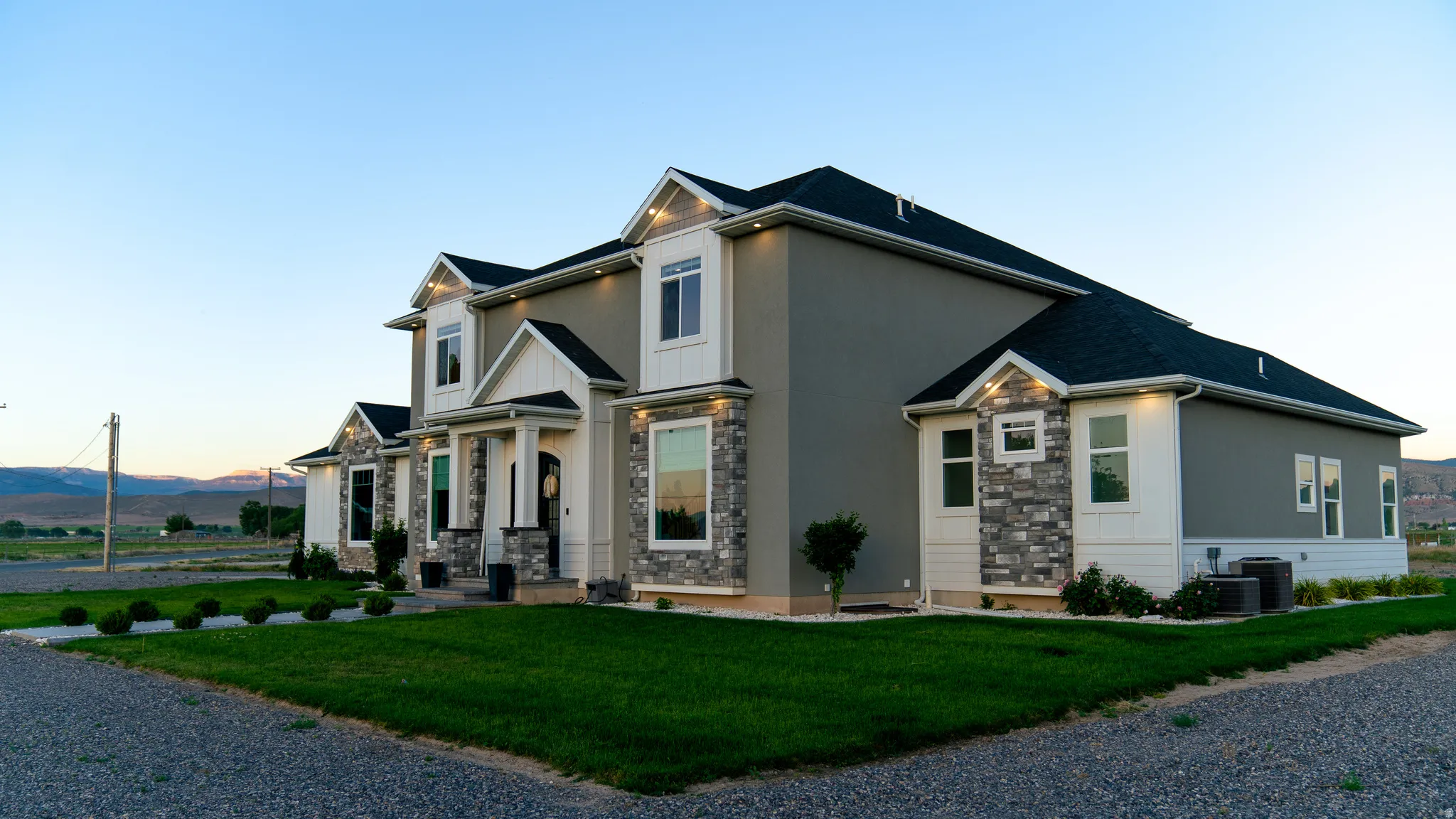 Contemporary two-story exterior featuring a stucco and stone facade, dark asphalt shingle roof, and white trim
