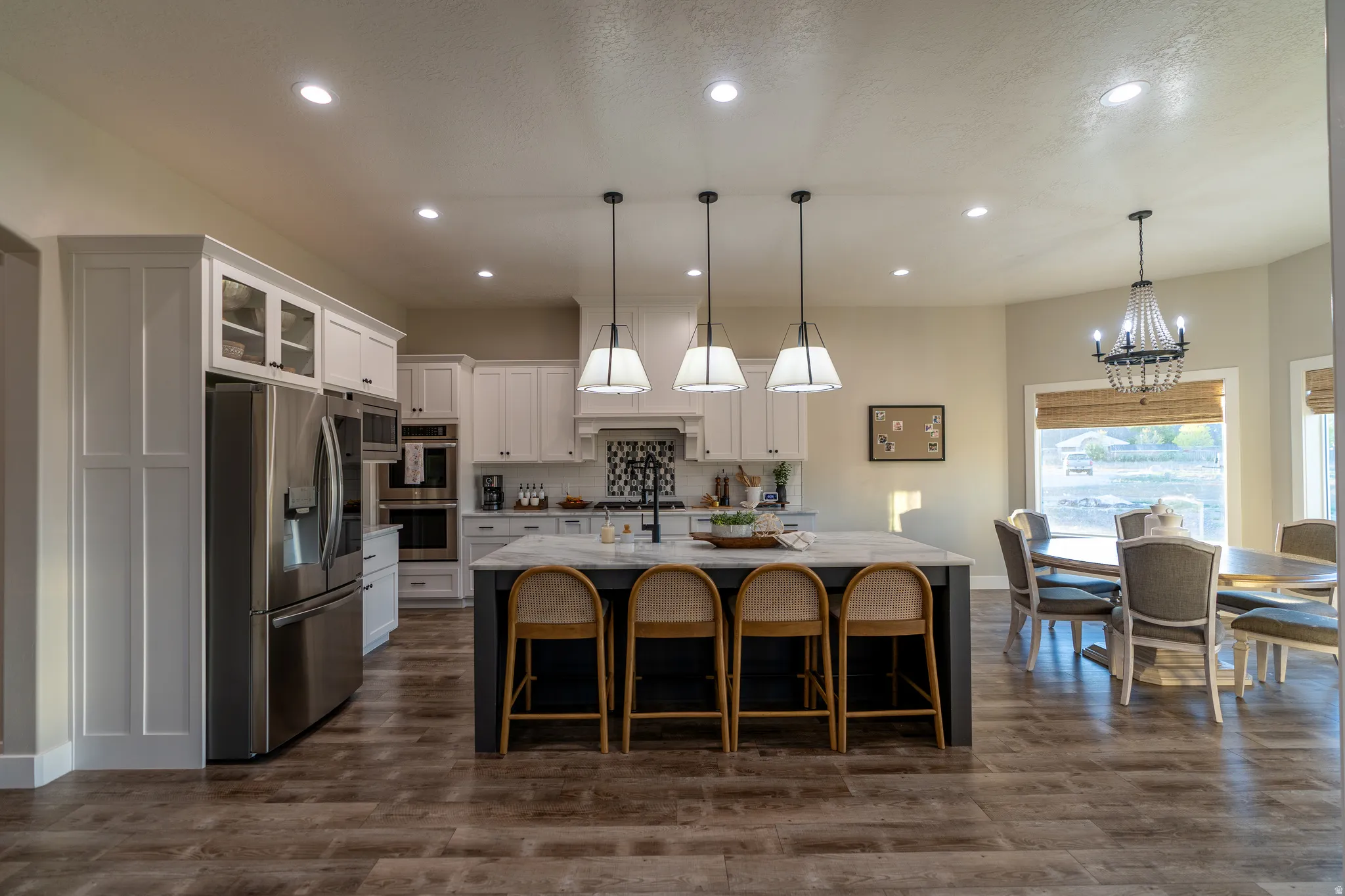 Open-concept kitchen featuring an oversized island with seating, pendant lighting, stainless steel appliances, and wood-finish flooring