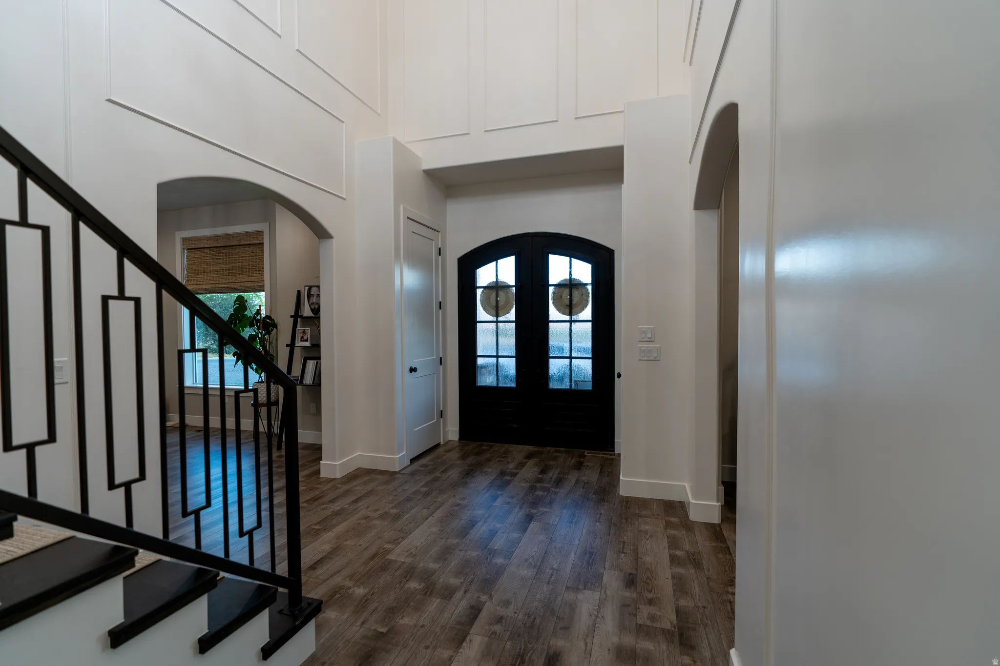 Entry foyer featuring arched doorways, wood-finish flooring, a modern black metal staircase railing, and a black arched glass-panel double door entrance