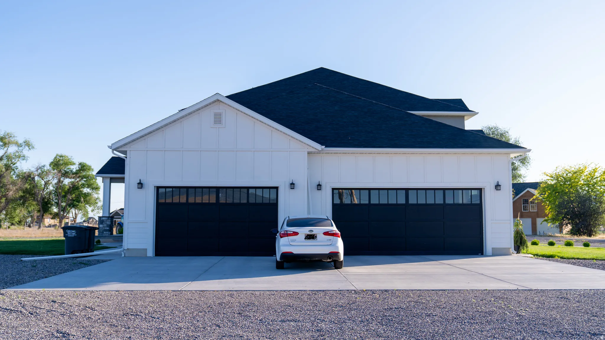 Modern farmhouse exterior featuring white board and batten siding, a dark shingle roof, a two-car garage with black paneled doors and upper windows, and exterior sconce lighting