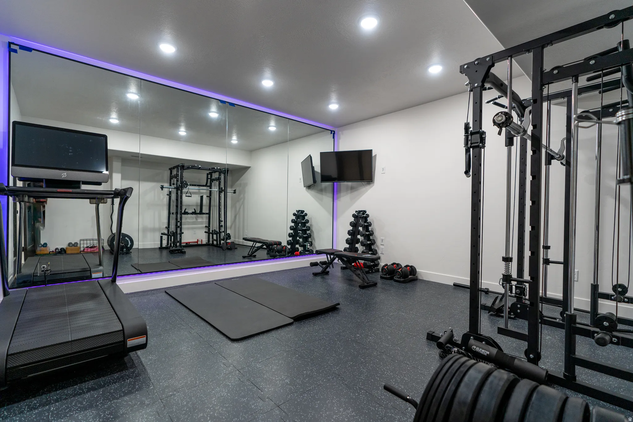 Dedicated fitness room featuring a full wall mirror with accent lighting, recessed ceiling lights, and durable rubber flooring