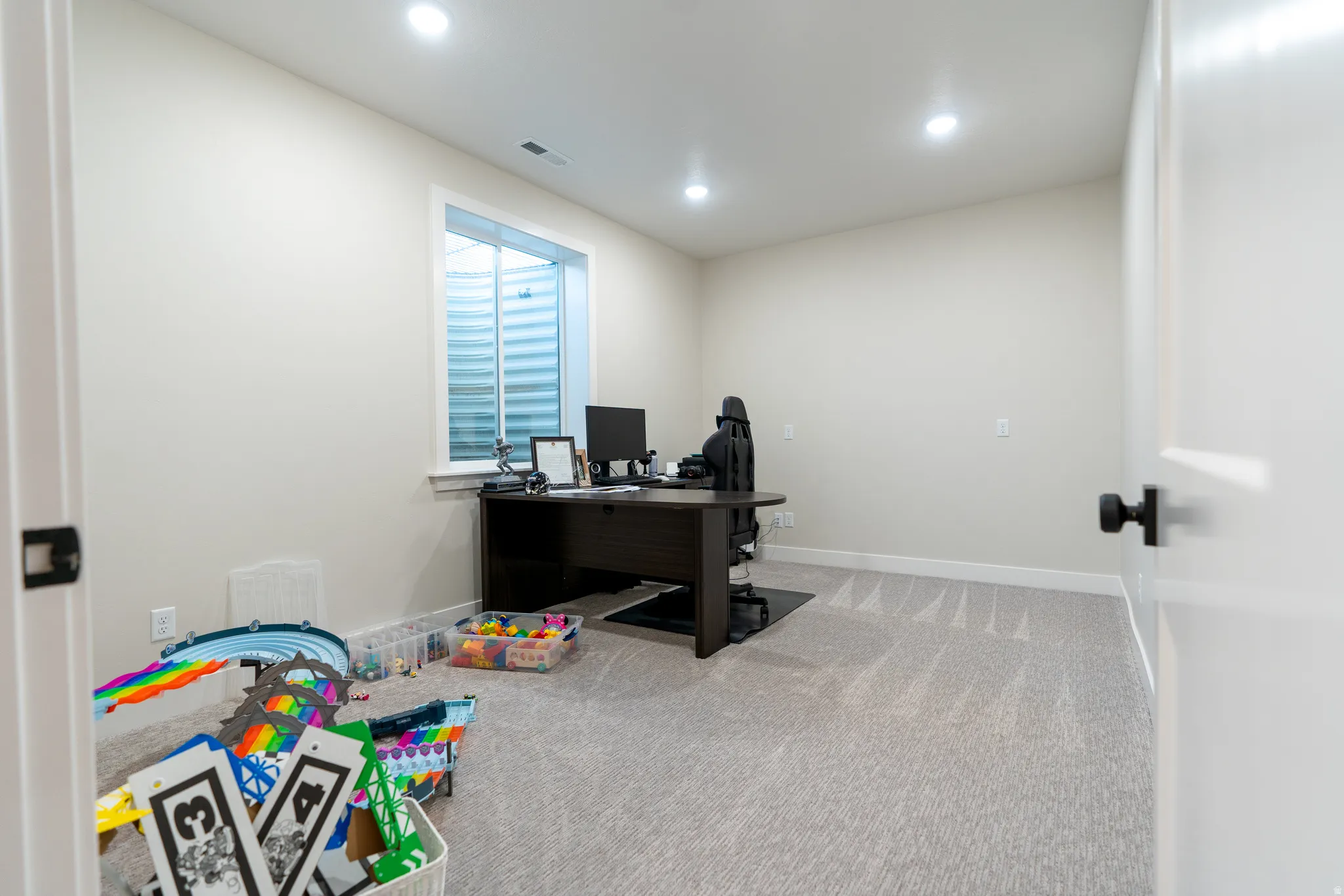 Finished room featuring light neutral walls, recessed ceiling lights, a basement window, and light grey carpet flooring