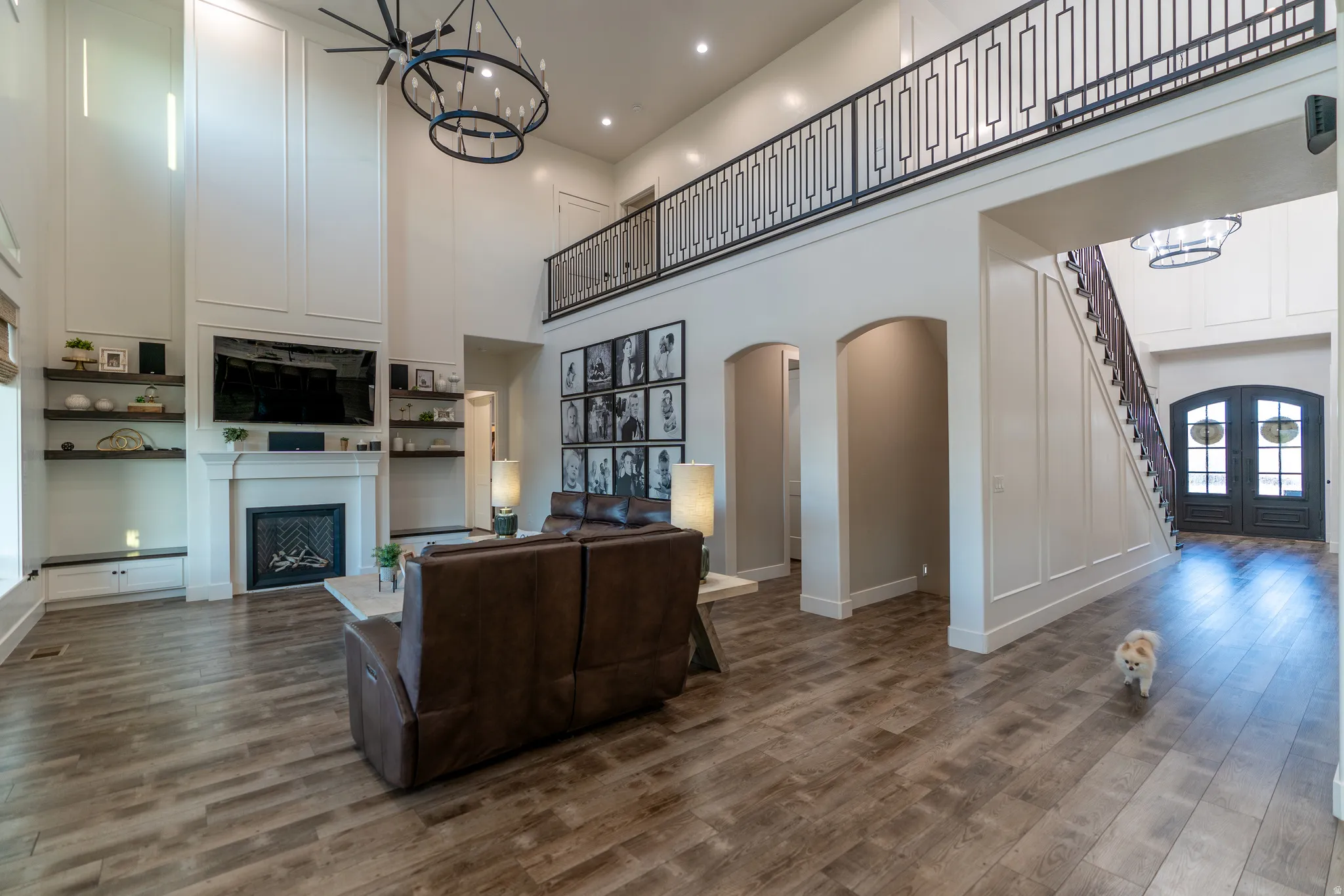 Two-story living area featuring wood-finish flooring, a white mantel fireplace, and built-in shelving
