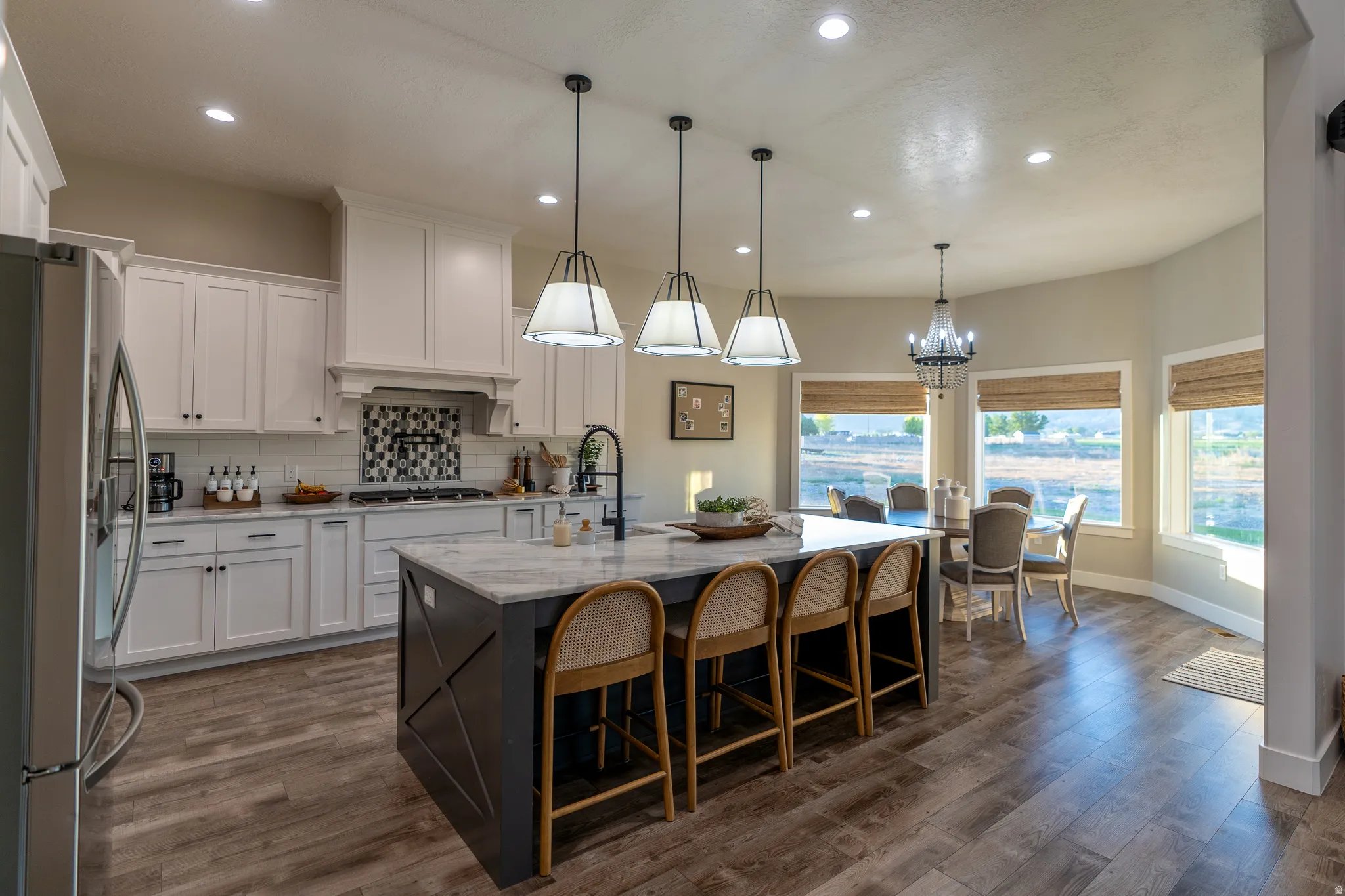 Open-concept kitchen featuring an oversized island with seating, pendant lighting, white cabinetry, a decorative backsplash, and wood-finish flooring