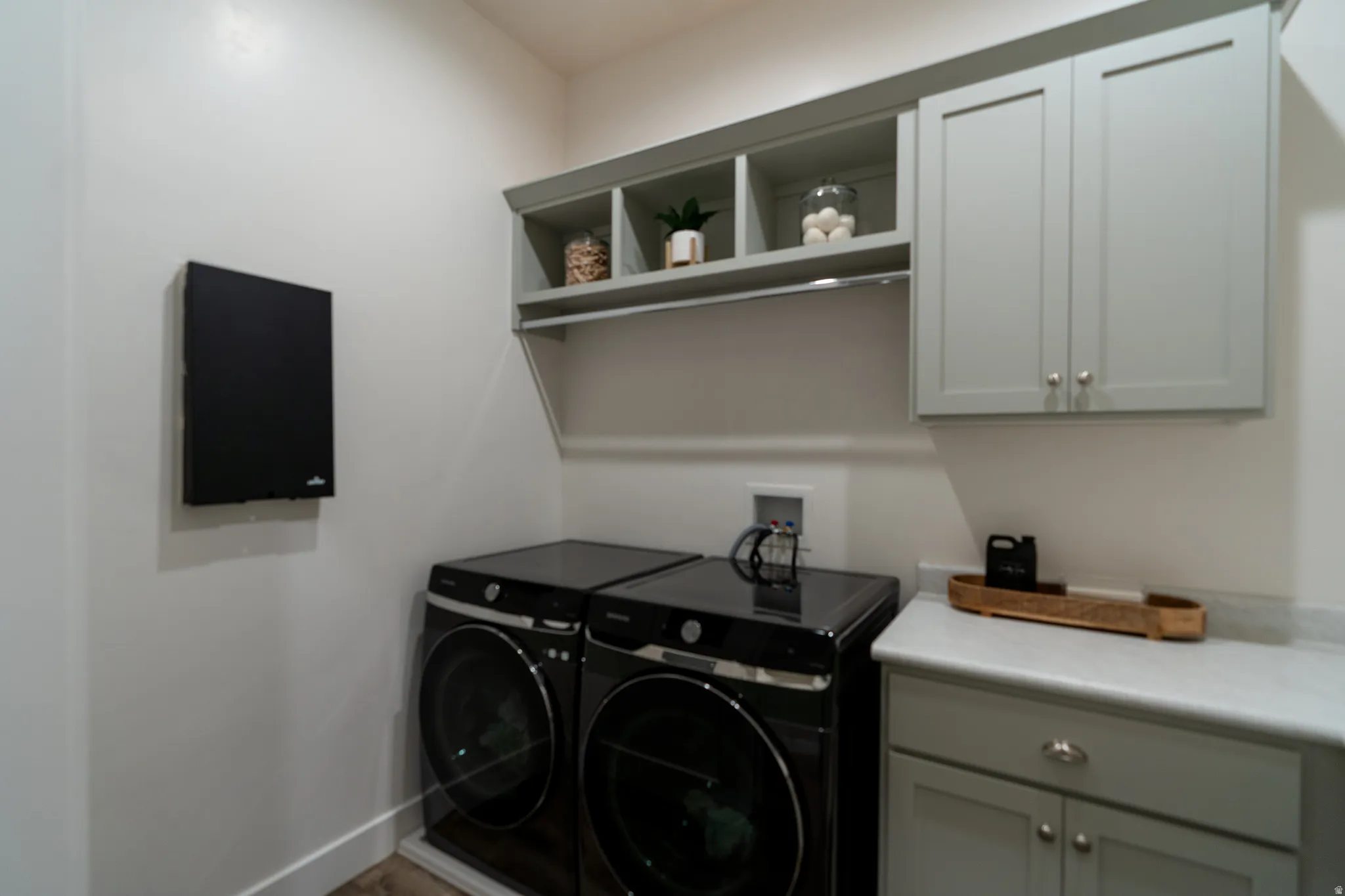 Dedicated laundry area featuring modern appliances, shaker-style cabinetry, open shelving, a countertop surface, and wood-finish flooring