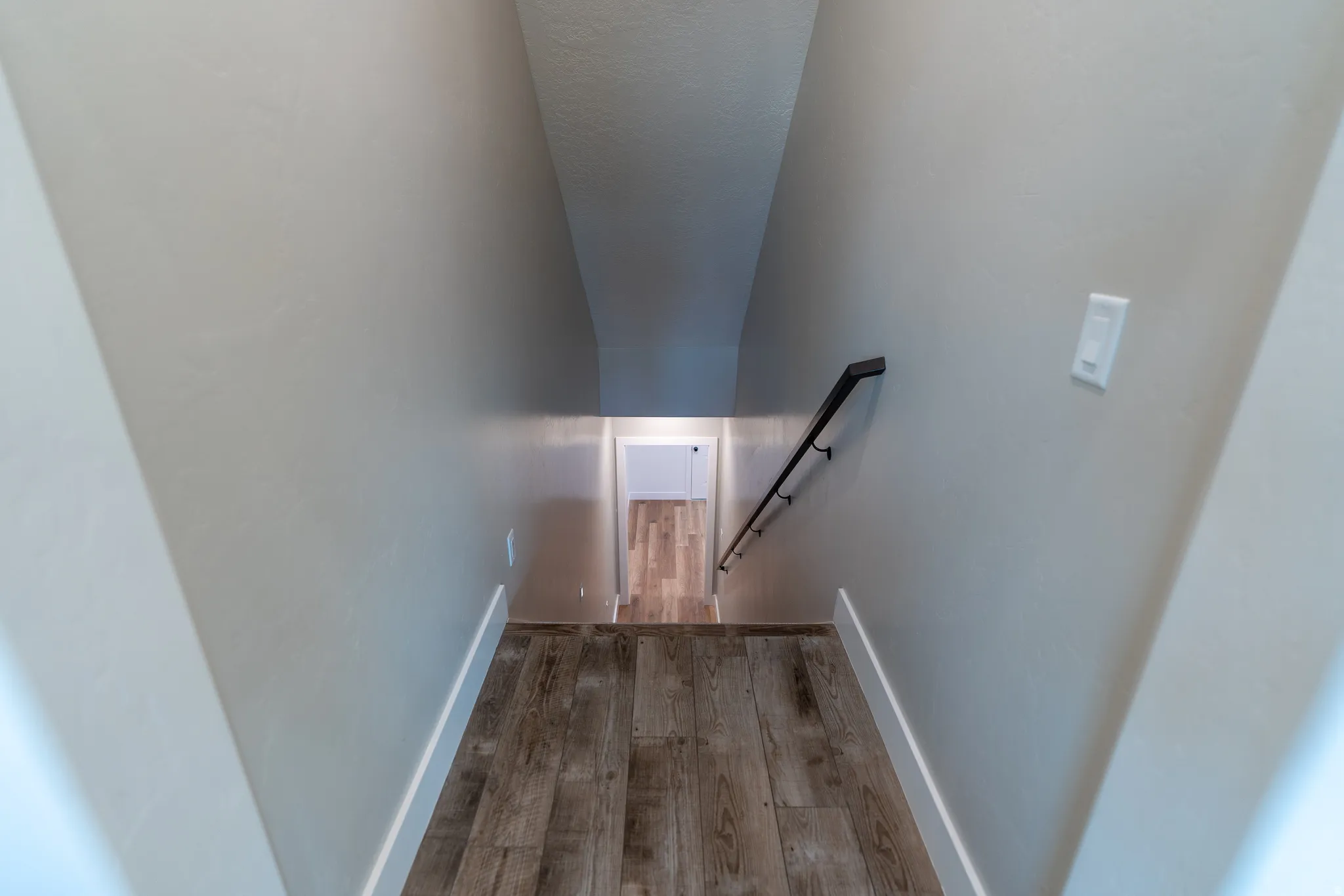 Stairway featuring wood-finish flooring, a contemporary black handrail, and light-toned wall paint