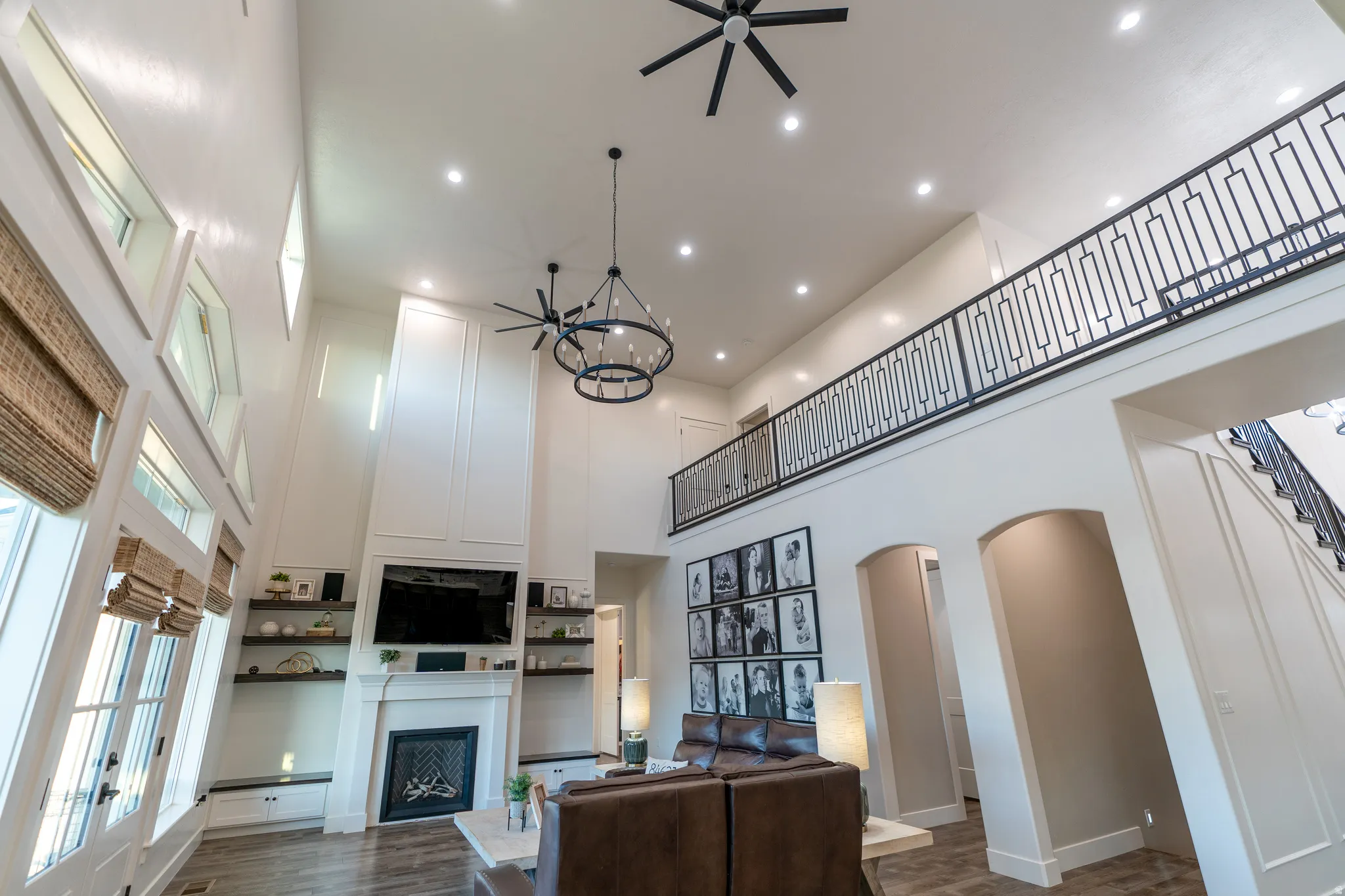 Two-story living area featuring a fireplace with white mantel, wood-finish flooring, and a second-story balcony with metal railing