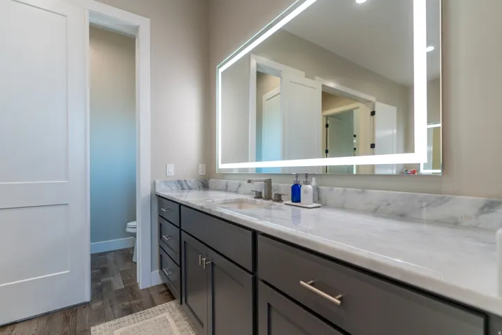 Vanity featuring a stone countertop, an integrated sink, a rectangular illuminated mirror, and dark-toned cabinetry with brushed nickel hardware