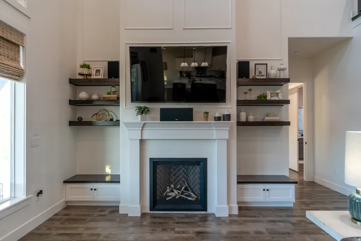 Modern living room featuring a tall white fireplace surround, built-in shelving, integrated lower cabinetry, and wood-finish flooring