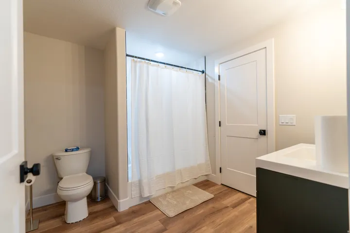 Full bathroom featuring wood-finish flooring, a white toilet, a shower with a white curtain, a flat-panel door with matte black hardware, and a vanity with a white countertop