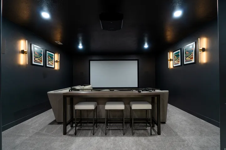 Dedicated media room featuring a large projection screen, dark-toned walls, recessed ceiling lighting, and wall-mounted sconces