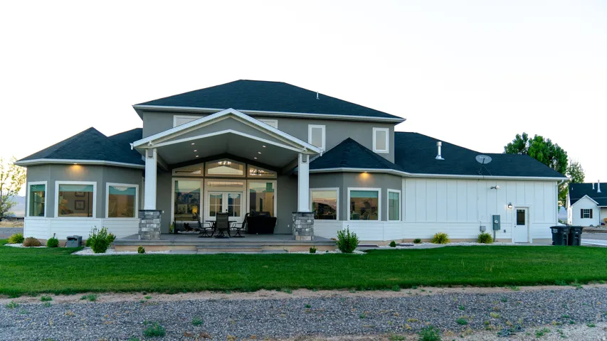 Rear exterior featuring a covered patio, multiple large windows, a bay window section, and a manicured lawn