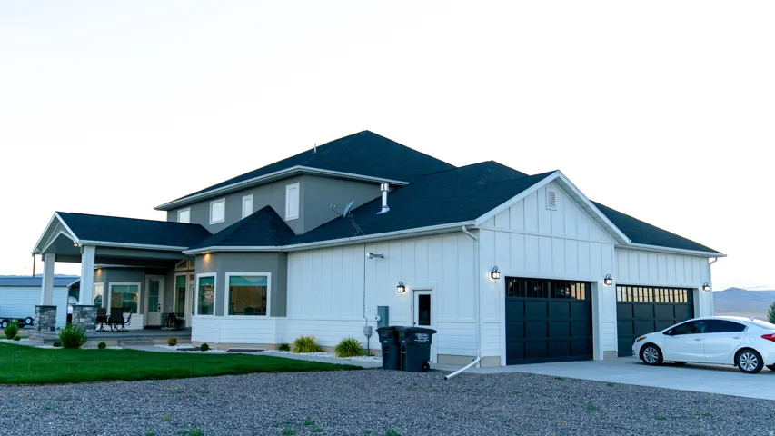 Contemporary two-story residence featuring a dark shingle roof, gray stucco siding, and white vertical paneling