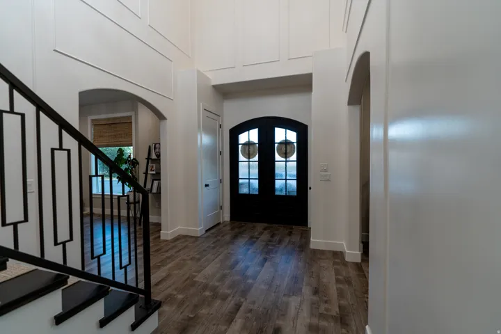 Entry foyer featuring arched doorways, wood-finish flooring, a modern black metal staircase railing, and a black arched glass-panel double door entrance