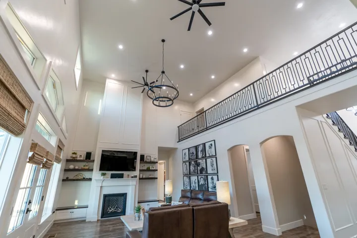 Two-story living area featuring a fireplace with white mantel, wood-finish flooring, and a second-story balcony with metal railing