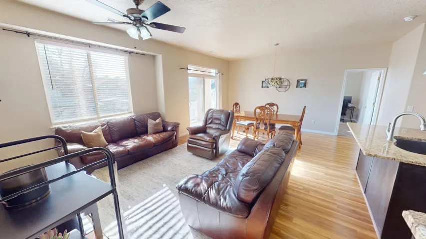 Open-concept living space featuring wood-finish flooring, a large window with horizontal blinds, and a ceiling fan with integrated lighting