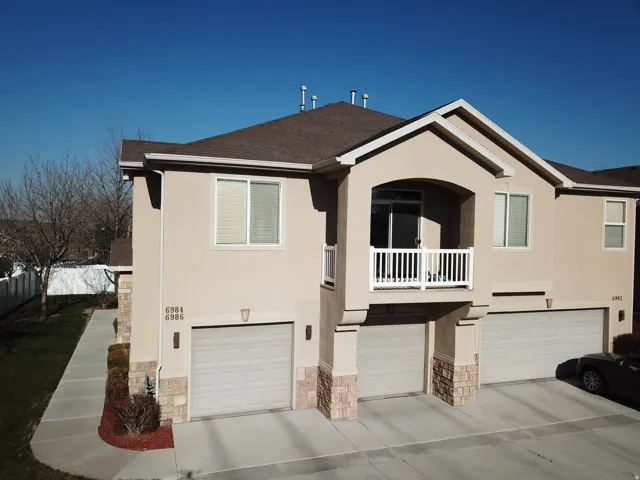 Stucco exterior with stone veneer accents, individual garage doors, and a second-story balcony with white railings