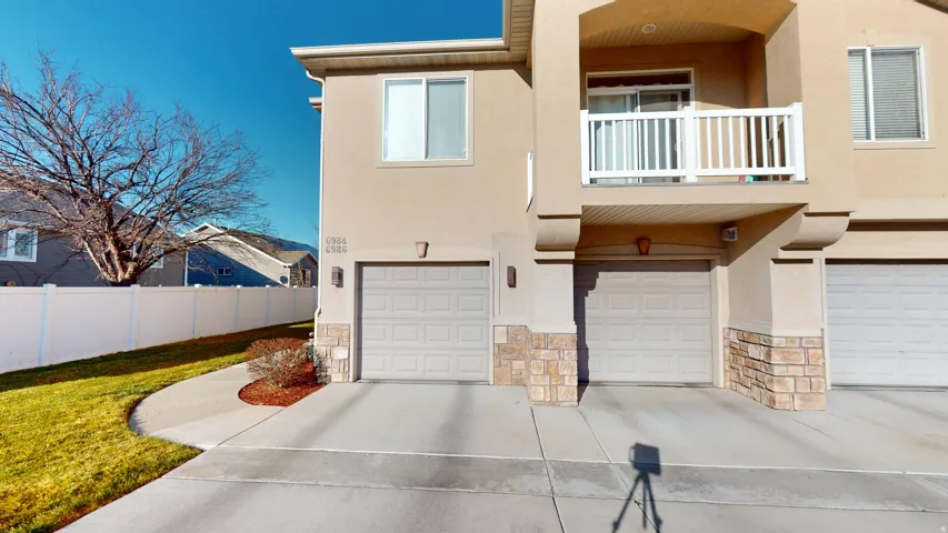 Multi-level exterior featuring light stucco siding, stone accents, two single-car garages, and a second-story balcony with white railing