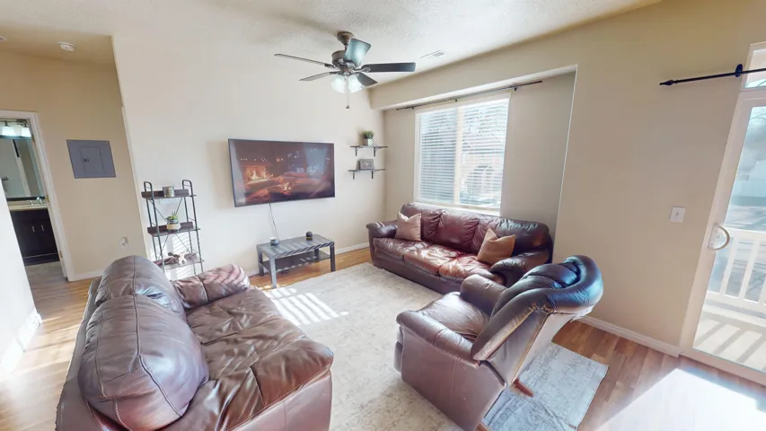 Spacious living area featuring light-toned walls, wood-finish flooring, and a ceiling fan